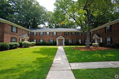 the front of a brick house with a lawn and trees